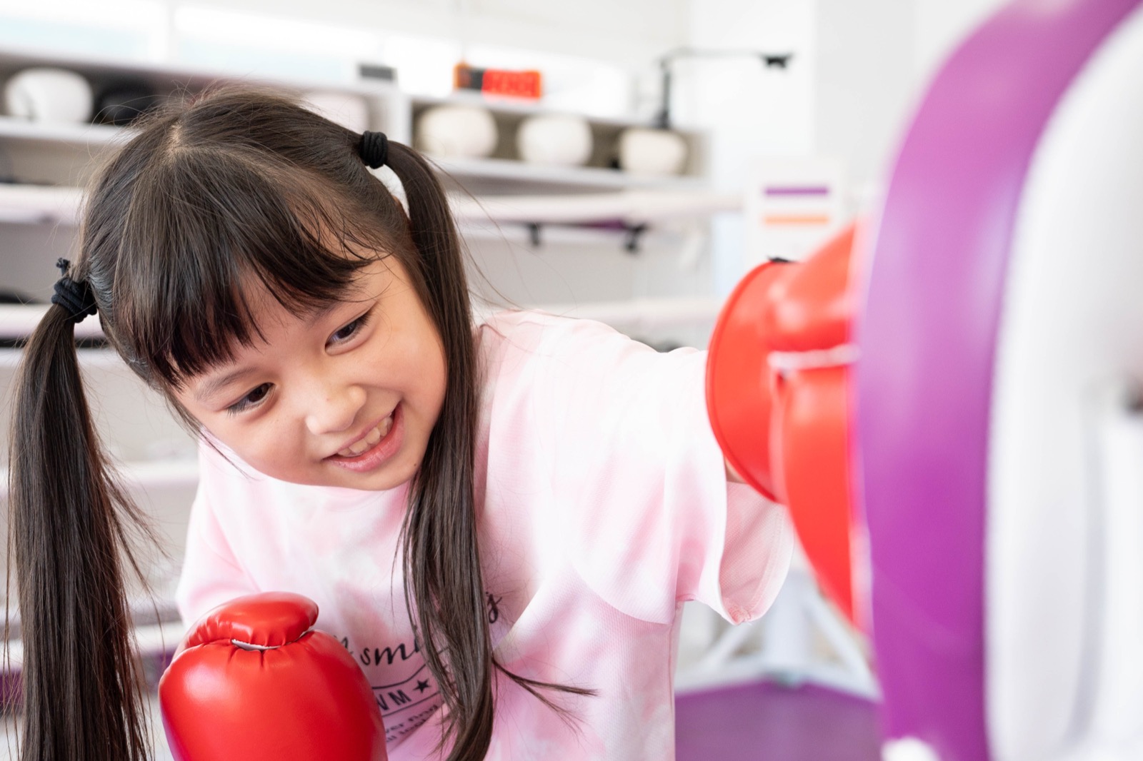 福岡 薬院のキッズ英会話English Fight Kidsのジムで、笑顔の小学生が明るい空間でミットにパンチし、奥で友達がラダーゲームをしているノンコンタクト指導風景